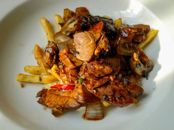 A flavorful Char Siu pork stir-fry, glazed in black bean sauce, served with sauteed vegetables and crispy french fries.