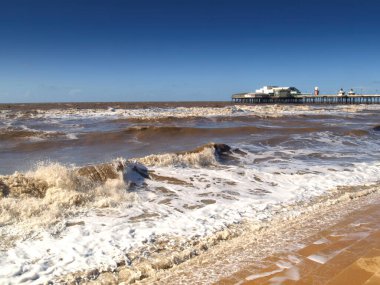 Dinamik okyanus dalgaları, güneşli altın plajda beyaz köpüğe dönüşür ve tarihi Kuzey İskelesi 'ne doğru yol alır..