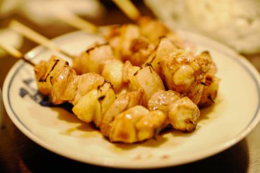 Lezzetli sosla parlayan üç mükemmel ızgara tavuk yakitori şişi klasik bir Japon seramik tabağında servis ediliyor..