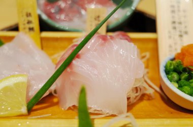 Taze dilimlenmiş beyaz balık sashimi, ahşap bir tabakta limon ve yeşil soğanla, tadını çıkarmaya hazır..