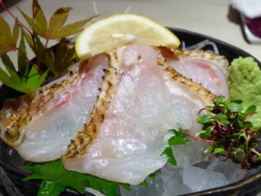 Nefis taze sashimi, kavrulmuş derisi olan narin çiğ balık, buzun üzerinde güzel bir şekilde sunulan bir limon dilimi, yeşil akçaağaç yaprakları, ve wasabi, bir gurme Japon lezzeti..