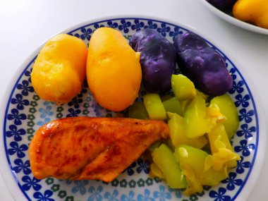 Izgara tavuk, sarı ve mor patates ve taze yeşil sebzelerden oluşan canlı ve dengeli bir yemek tabağı..