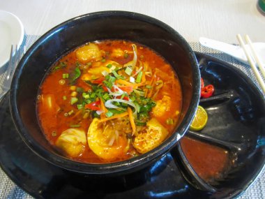 Taze malzemelerle süslenmiş renkli ve aromatik bir kase baharatlı Laksa Lemak şehriye çorbası zengin ve otantik bir Malezya mutfağı deneyimi sunar..