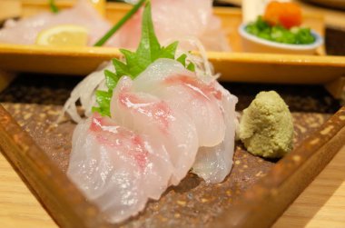 Sanatsal olarak hazırlanmış taze beyaz balık sashimi bir tutam wasabi ve dekoratif yeşil yaprakla sunuluyor..