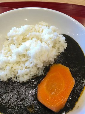 Tüylü pirinç, koyu köri sosu ve kırmızı-kahverengi ahşap tepside duran parlak turuncu somon dilimiyle dolu beyaz bir kasenin yakın çekimi..