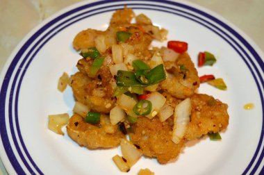 Üzerinde soğan, yeşil ve kırmızı biber ve biber bulunan hafif dövülmüş karides mavi çizgili beyaz bir tabakta servis ediliyordu..