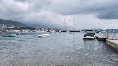 Kasvetli deniz limanındaki dalgalı sular, kayıklar ve dağ manzaralı dramatik sahil limanı.