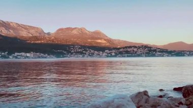 coastal mountains at golden hour sunset soft pastel sky over tranquil bay with gentle waves lapping rocky