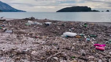 pebble beach strewn with plastic debris and styrofoam near small island, close foreground shows pink sandal and white foam