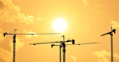 Sabah vakti sarı gökyüzü olan kule inşaat vinçlerinin siluetleri