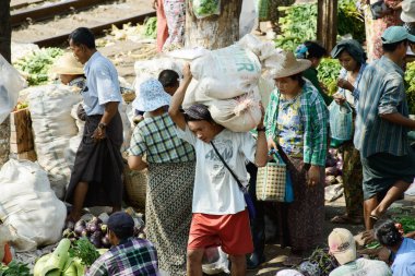 02 / 22 / 2014 Yangon, Myanmar Bir adam Yangon tren istasyonu pazarında ağır bir çuval taşıyor, satıcıların doğrudan rayların yanında sebze ve mal sattığı yerde. Görüntü, istasyonda meydana gelen günlük faaliyetleri ve gayri resmi ticareti belgeliyor. .