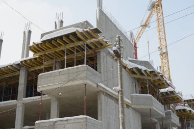 Çok katlı beton bir yapı hafif kar yağışı altında duruyor. Açık zeminleri, resmi işleri ve soğuk hava koşullarında binanın üzerinde yükselen bir vinci gösteriyor..