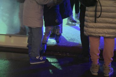 Romanya 'daki Craiova Noel Pazarı' nda kış kıyafetleri ve buz pateni giyen ziyaretçiler aydınlık bir buz pateni pistinin kenarında duruyorlar.