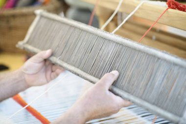 Bir zanaatkar, ahşap dokuma tezgahında el yünü örerken warp ipliklerini sıkıştırmak için bir tezgah çırpıcı tutar..