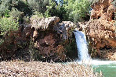 Tavira, Algarve, Portekiz 'deki yeşil bitki örtüsüyle çevrili kırmızı kayalıklara tırmanan kişi ile Pego do Inferno Şelalesi manzarası. Aydınlık bir yaz gününde.
