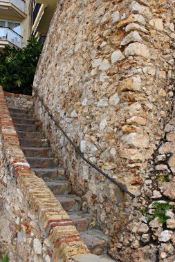 İspanya, Barselona 'daki tarihi Sitges şatosunun yanında kırsal duvarlı eski taş merdiven. Ortaçağ mimarisi ve geleneksel Akdeniz inşaat detayları, antik taş işçiliği ile Katalan kıyı kasabasındaki kentsel çevreyi harmanlıyor..