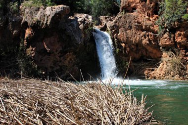 Portekiz, Tavira 'daki Pego do Inferno şelalesinin canlı manzarası turkuaz suları, engebeli turuncu kayalıkları ve çağlayanın etrafındaki yemyeşil bitkileri gösteriyor. Bu gizli Algarve cennetinin el değmemiş doğal güzelliğini ve dingin atmosferini yakalıyor..