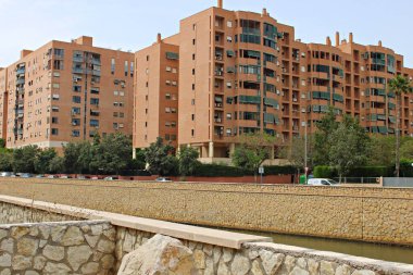 Alicante, İspanya 'daki modern apartman kompleksi. İçinde balkonları, yeşil tenteleri ve taş duvarlı kanalı çevreleyen ağaçları olan terracotta renkli binalar var..
