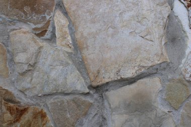 Düzensiz bir doğal taş duvarın detaylı dokusu bej, lacivert, gri ve kahverengi tonlarda, ve sert harç ile birleştirilmiş. Mimari yüzeyler, inşaat malzemeleri, kırsal cepheler ve yüksek çözünürlüklü arka planlar için ideal