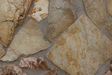 Gri harç şeklinde düzensiz levhaları olan doğal kahverengi taş duvar dokusu, organik desenler, engebeli yüzeyler ve toprak renkleri sergiliyor. Mimari altyapı, inşaat malzemeleri, kırsal tasarım, dış cepheler ve taş dokular için ideal