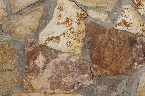 Gri çimento harcı ile birleştirilmiş çok renkli levhalar içeren düzensiz taş bir duvarın detaylı dokusu. Mimari altyapılar, inşaat malzemeleri, kırsal yüzeyler, doğal taş kalıpları ve yüksek çözünürlüklü doku kaynakları için ideal