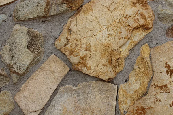 Gri havan topları, ince mineral damarlar, yıpranmış yüzeyler, topraksı tonlar ve kırsal yapı desenleri içeren büyük düzensiz bej ve lacivert levhalar içeren ayrıntılı doğal taş duvar dokusu. Arka planlar için ideal.