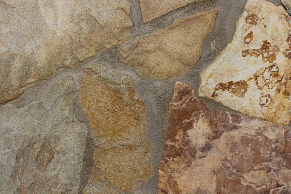 Çok renkli doğal taş duvar dokusu, bej, kahverengi, toprak rengi ve gri gibi toprak tonlarda düzensiz plakalar içerir ve sert havan topuyla birleştirilir. Mimari arka planlar, inşaat malzemeleri, kırsal cepheler ve dekoratif taş desenler için ideal