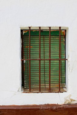 Endülüs 'te beyazlatılmış bir duvarda yaşlı, yeşil ahşap panjurlu bir pencere, soyulmuş boyalar, yıpranmış dokular ve geleneksel mimari unsurlar sergileniyor, miras cephesi ve Endülüs sokaklarının teması için mükemmel. 