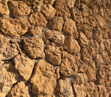 Yıpranmış taş duvar dokusu, ılık tonlarda düzensiz sert kayalar, doğal aşınma, engebeli yüzeyler ve organik desenler gösteriyor. Mimarlık, inşaat, restorasyon ve kırsal tasarım projeleri için ayrıntılı yakın plan ideal