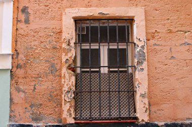 Eskimiş bir Endülüs duvarında eski bir pencere, şeftali rengi boyayla soyulmuş alçı ve taş tabakaları ve dokulu çürük; zamanın geçişini ve geleneksel İspanyol mimarisinin ayırt edici çekiciliğini yakalayan kırsal bir ön cephe.