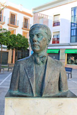 İspanyol şair Luis Cernuda 'nın bronz büstü, 27 Nesil' in ünlü yazarı onuruna Dos Hermanas, Seville, İspanya 'da halka açık bir meydanda sergilenirken, arka planda edebiyat mirası ve kültürel hafızayı sembolize eden şehir mimarisi yer aldı.