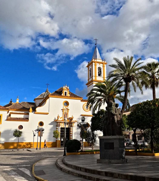 Iglesia de Santa Maria Magdalena çan kulesi, palmiye ağaçları ve Plaza de los Jardines 'deki anıt, Endülüs, İspanya, tarihi beyaz ve koyu renkli kilise dramatik mavi gökyüzü altında bulutlar, kentsel kültür simgesi