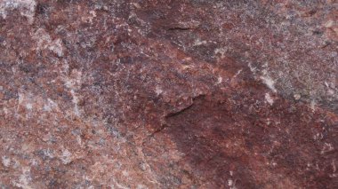 Kırmızımsı kahverengi taştan yapılmış, pürüzlü, düzensiz ve doğal jeolojik dokusunu gösteren engebeli bir duvar veya uçurumun detaylı, soyut bir yakın çekimi..
