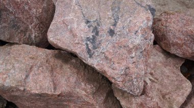 İnşaat veya tasarım için uygun kaba, parçalanmış ve doğal kaya dokusunu gösteren büyük, pembe gri granit taşlar kümesi..