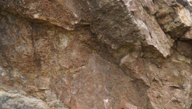 Güçlü çapraz çizgiler ve çatlaklar gösteren kahverengi bir kaya yüzeyinin yakın çekimi, engebeli jeolojik yapıyı ve doğal hava koşullarını vurguluyor..