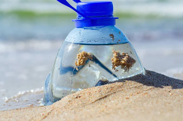 Plastic bottle in beach sand. Plastic pollution of the oceans concept. Package garbage on the shore. Global warming problem. Pet bottle of fresh water is on the sand by the sea.