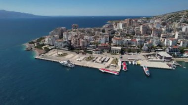 Saranda limanı ve körfezinin geniş insansız hava aracı görüntüsü rıhtımda, rıhtımda ve yoğun sahil şehrinde feribotları var. İyon Denizi üzerinde açık hava.