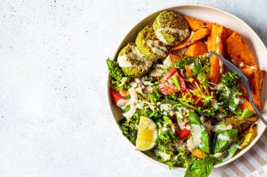 Falafel salata kasesi. Vejetaryen yemek tabağı - fırınlanmış nohut pirzolası fırında tatlı patates ve sebze salatası ile beyaz tabakta.