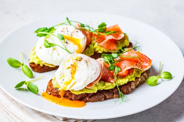 Somonlu tost, haşlanmış yumurta ve beyaz tabakta avokado. Somonlu haşlanmış yumurta ve çavdar ekmekli guacamole..