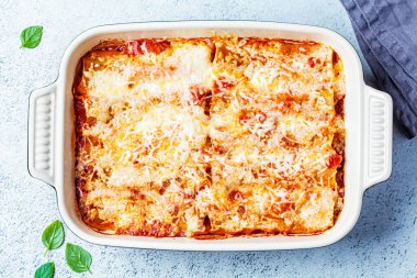 Geleneksel cannelloni et, domates sosu ve peynirli, kabartma kabında, gri arka planda. İtalyan mutfağı kavramı.