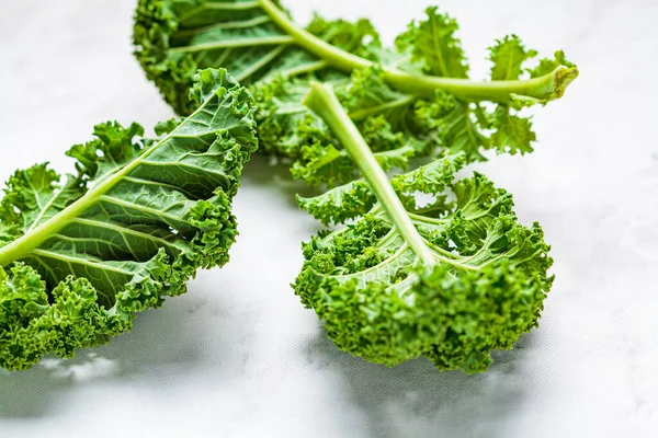 Fresh green kale salad leaves on white marble background.