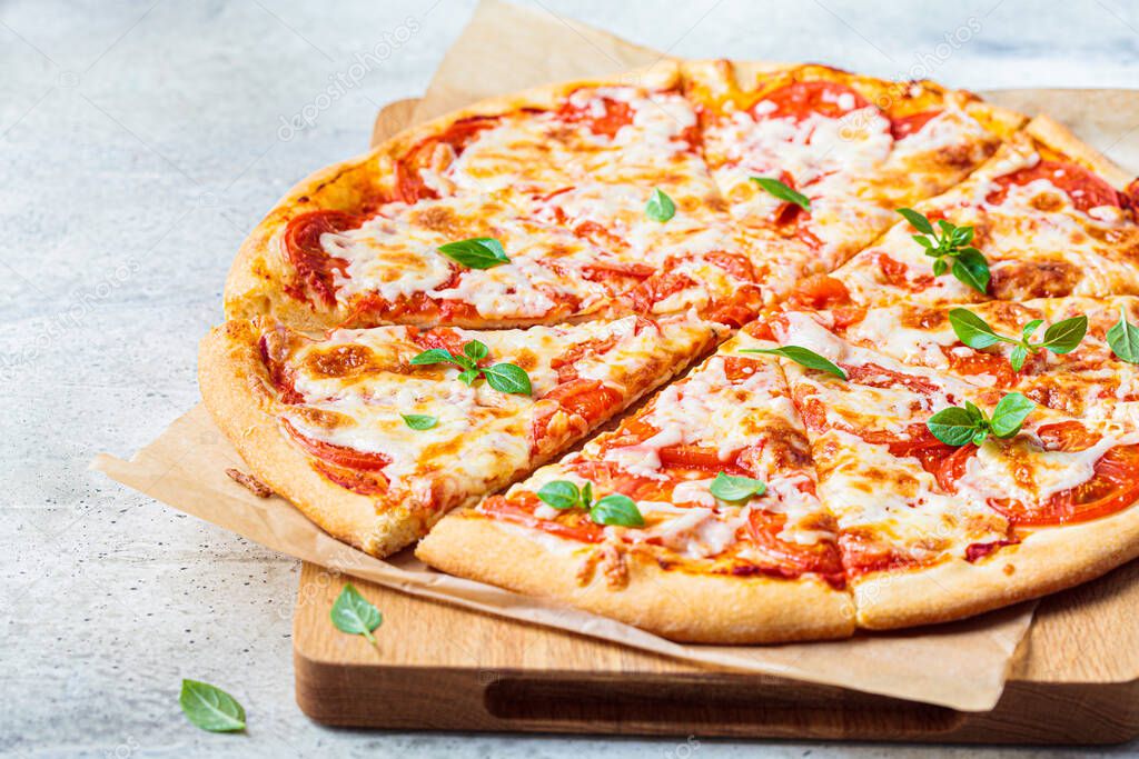 Classic pizza margarita with mozzarella, tomato and basil on a wooden board. Italian food concept.