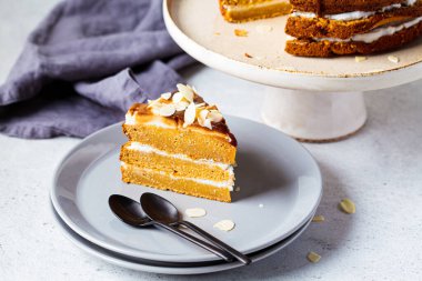 Gri tabakta bir parça vejetaryen keki. Beyaz kremalı, karamel ve fındıklı ev yapımı havuçlu kek..