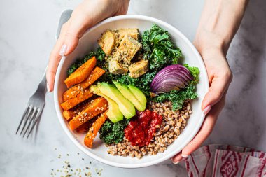 Fırında sebze, avokado, tofu ve karabuğday kasesi. Lahanalı vejetaryen öğle yemeği salatası, fırında tatlı patates, tofu, karabuğday ve avokado. Vegan kavramı.