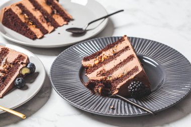 Gri bir tabakta böğürtlenli çikolatalı kek parçaları, beyaz mermer arka plan. Vejetaryen tatlı konsepti.