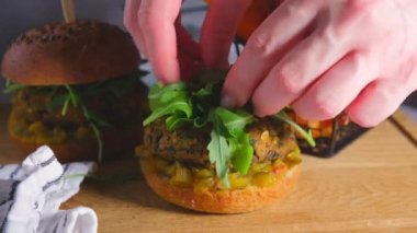 Kadın elleri sebzeli, roka ve hardal soslu vejetaryen mercimek burgeri pişiriyor..