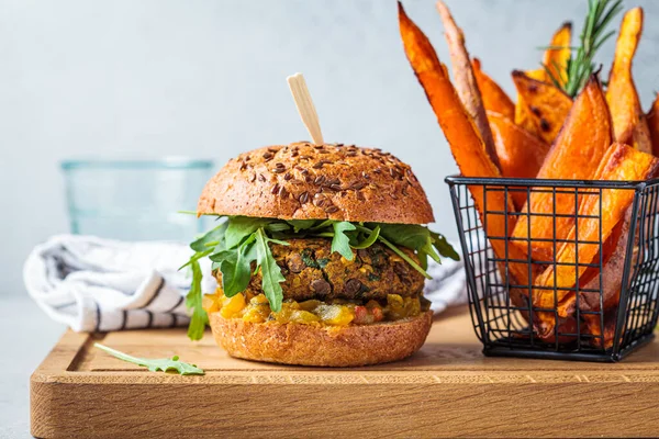 Vegan lentil burger with arugula, mustard sauce, fresh vegetables and sweet potato fries on a wooden board. Vegan food concept.