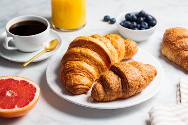 Kahvaltı konsepti. Böğürtlenli taze kruvasan, bir fincan kahve ve beyaz mermer arka planda bir bardak portakal suyu..