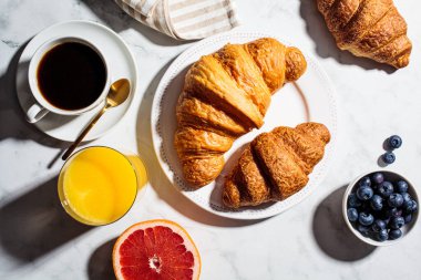 Kahvaltı konsepti. Böğürtlenli taze kruvasan, bir fincan kahve ve beyaz mermer arka planda bir bardak portakal suyu..