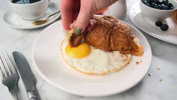 Croissant para comer a mano con huevo frito en plato blanco. Concepto de desayuno. — Vídeo de stock